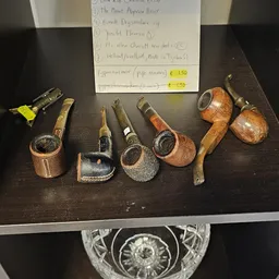 Collectie antieke houten pijpen met verschillende vormen en kleuren, uitgestald op donker oppervlak met prijskaartjes