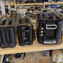 Drie zwarte elektrische koffiezetapparaten op houten tafel in kringloopwinkel