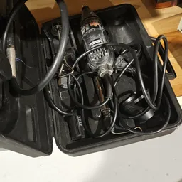 Zwarte plastic tas met elektrische apparaten en snoeren, waaronder een boormachine