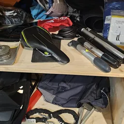 Fietsonderdelen en accessoires op een houten tafel, waaronder een zwart zadel, remmen en andere componenten