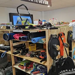 Houten stellingen met sportspullen, onder meer rollen, fitness-apparaten en zwart-oranje sportuitrusting