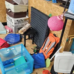 Diverse gebruikte huishoudelijke artikelen en speelgoed op de winkelvloer, waaronder plastic bakken, stoelen en ballonnen