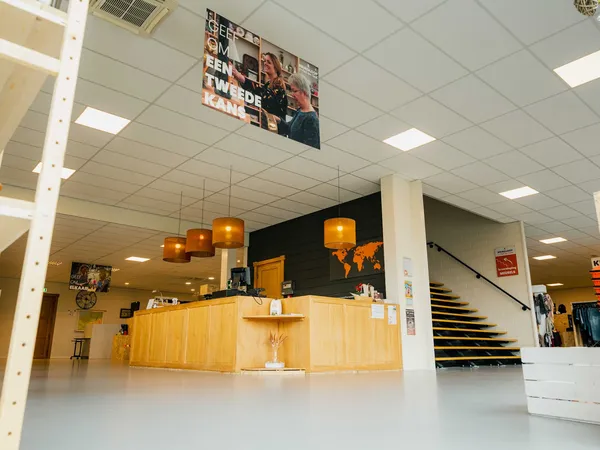 Winkelbalie met houten front en oranje hanglamp, trappen en stellingen zichtbaar in kringloopwinkel