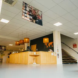 Winkelbalie met houten front en oranje hanglamp, trappen en stellingen zichtbaar in kringloopwinkel