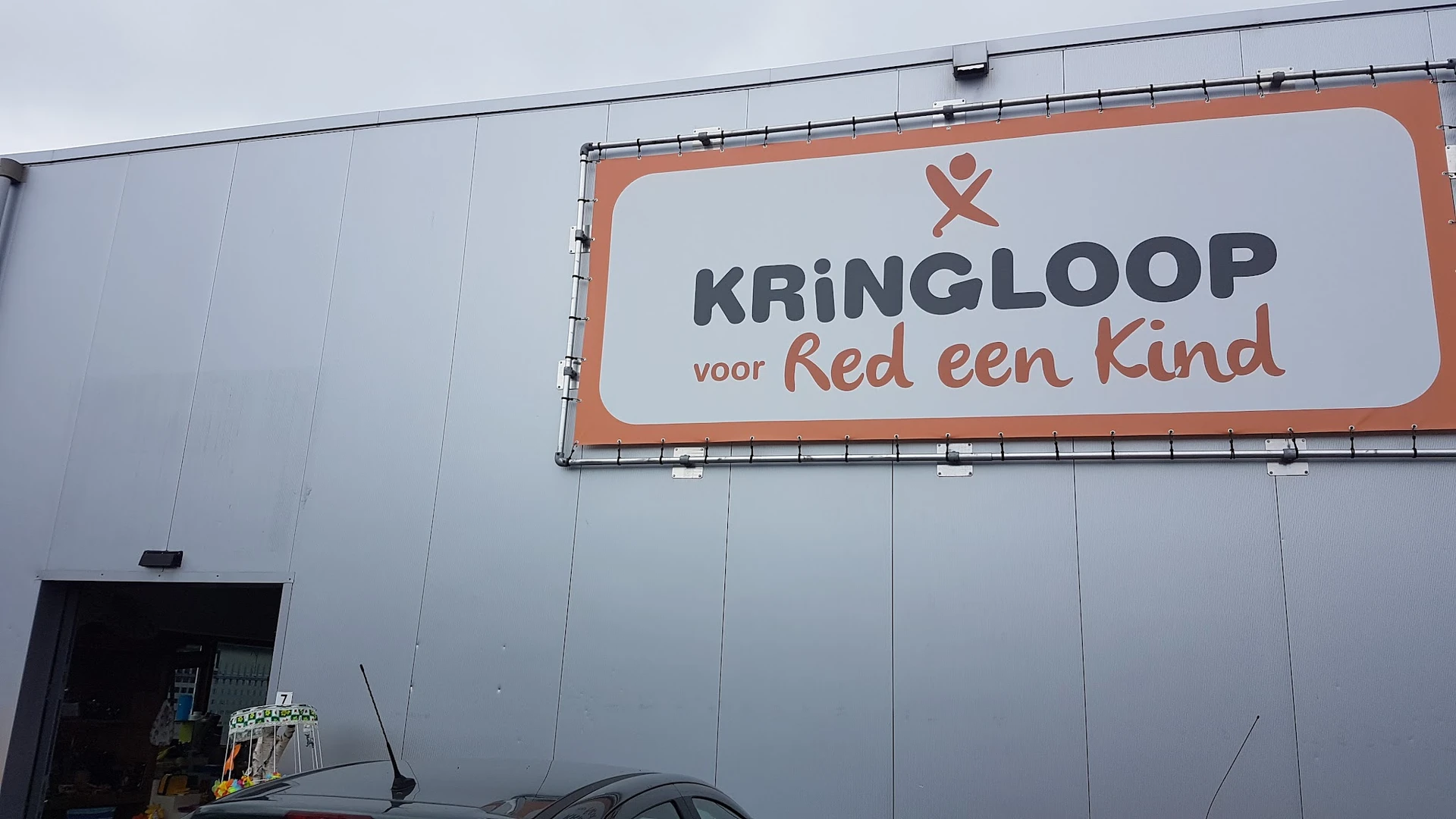 Gevel van kringloopwinkel met oranje en wit logo 'Kringloop voor Red een Kind'