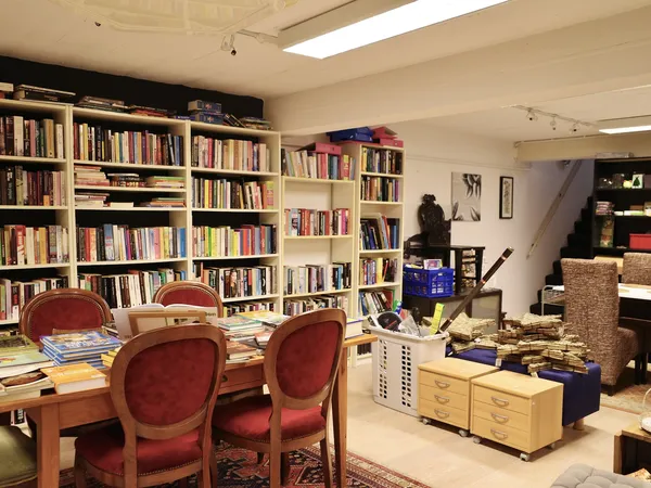 Boekenrekken vol tweedehands boeken, rode stoelen bij tafel, katvanger en diverse meubels in kringloopwinkel