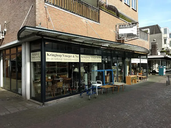 Winkelgevel van kringloopwinkel aan het Dorpsplein met grote ramen en blauw/groene stoelen buiten