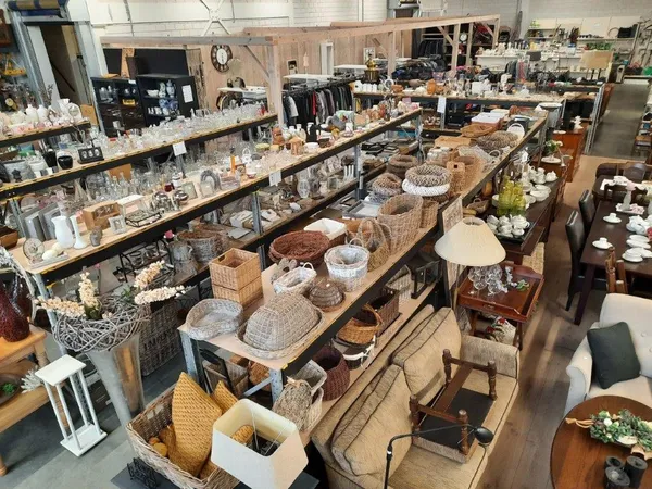 Overzicht van de winkelruimte met tafels vol huishoudspullen, servies, decoratie en secondhandartikelen