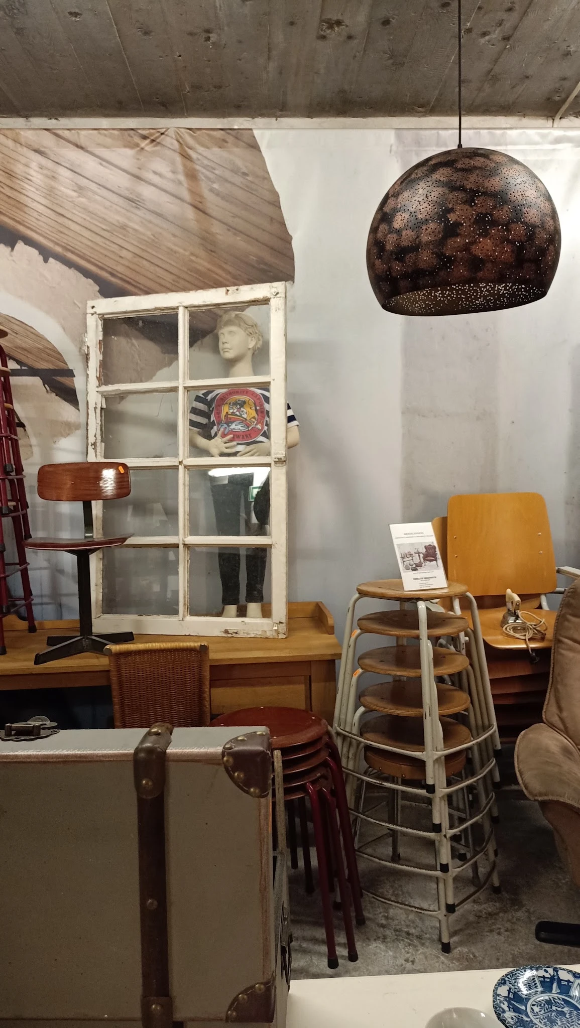 Diverse meubels en huishoudartikelen uitgestald in een kringloopwinkel, waaronder stoelen, een raam en decoratieve voorwerpen