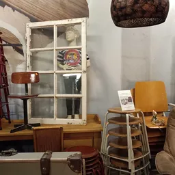 Diverse meubels en huishoudartikelen uitgestald in een kringloopwinkel, waaronder stoelen, een raam en decoratieve voorwerpen