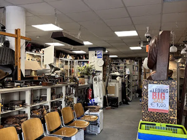 Winkelvloer van kringloopwinkel met stellingen, diverse spullen, stoelen en hangartikelen