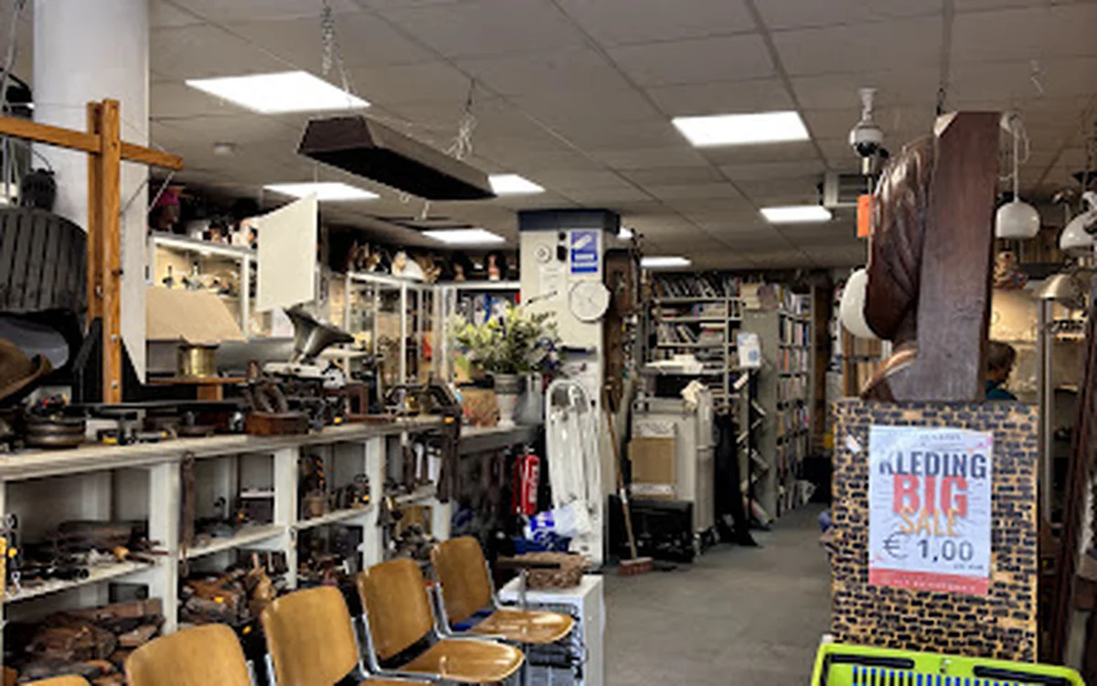 Winkelvloer van kringloopwinkel met stellingen, diverse spullen, stoelen en hangartikelen