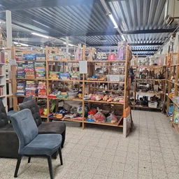 Winkelvloer met houten stellingen vol boeken, speelgoed en diverse spullen, met een zwarte stoel op de voorgrond