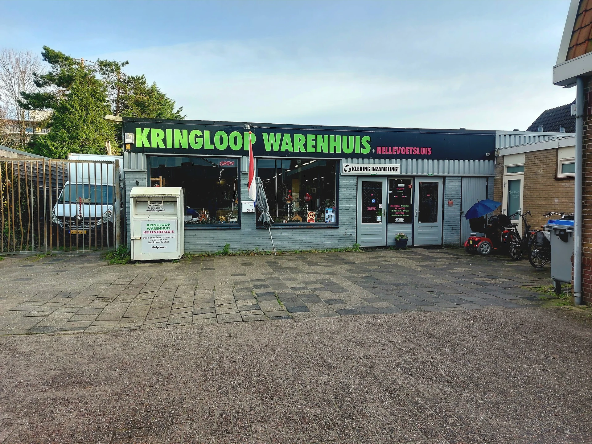Voorgevel van kringloopwinkel met groene letters en zwart pand aan parkeerterrein