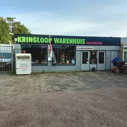 Voorgevel van kringloopwinkel met groene letters en zwart pand aan parkeerterrein