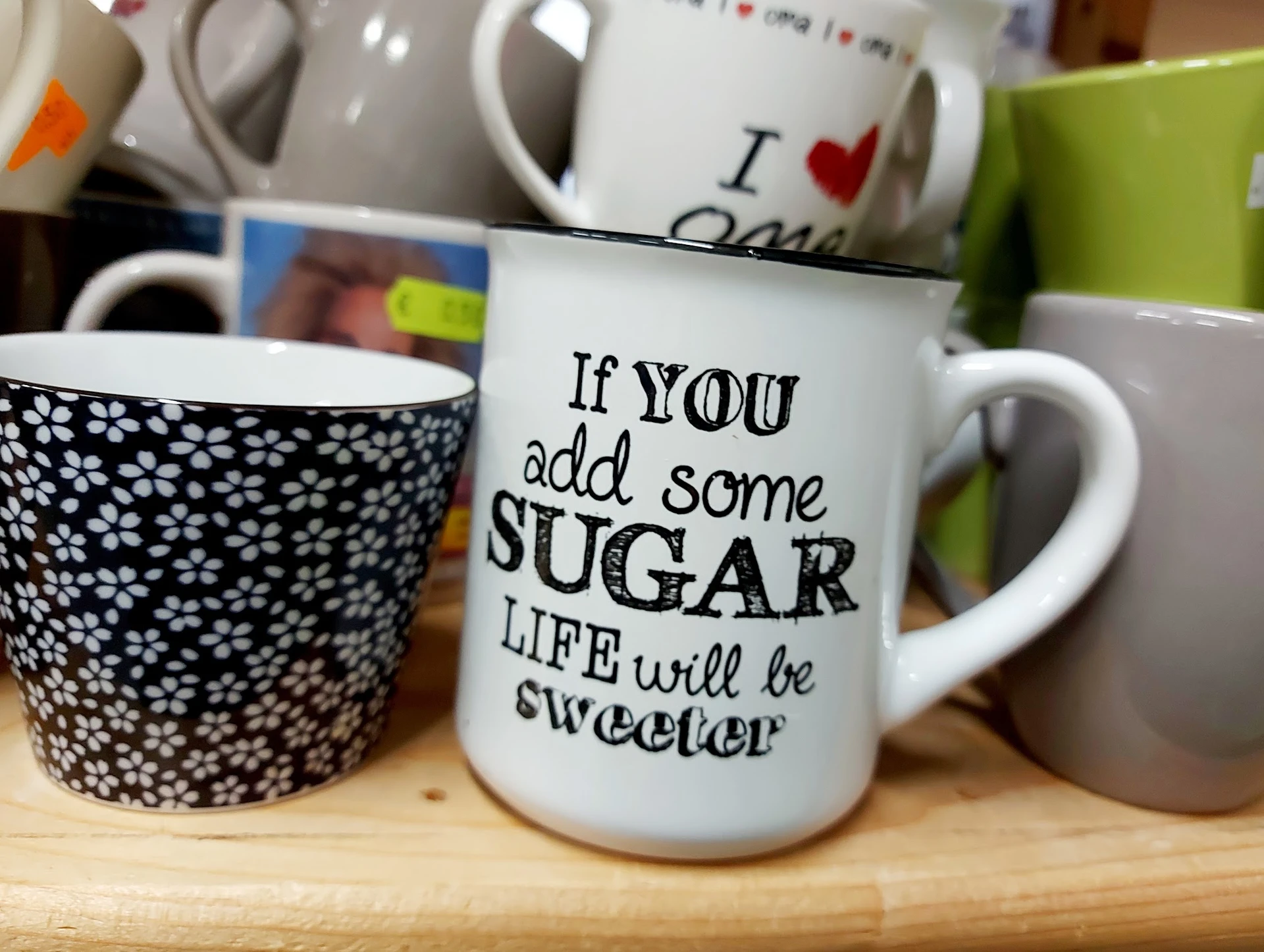 Drie koffiemugs met opdruk, waaronder één met tekst 'If you add some SUGAR LIFE will be sweeter'