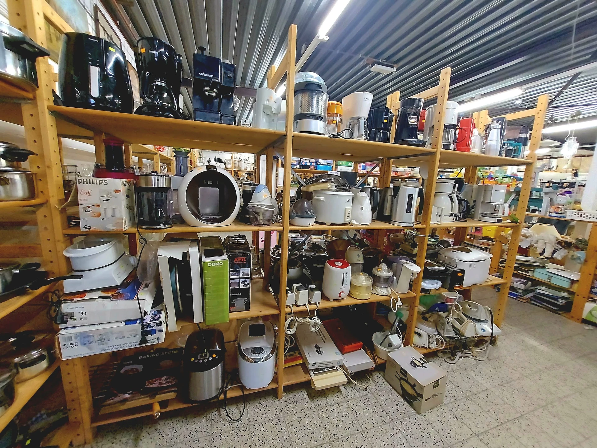Houten stellingen vol met huishoudelijke apparaten en elektronica in een kringloopwinkel