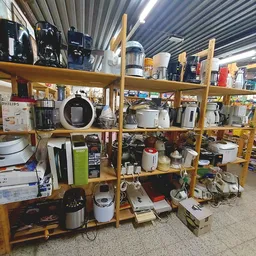 Houten stellingen vol met huishoudelijke apparaten en elektronica in een kringloopwinkel