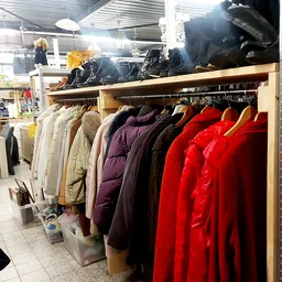 Rekken met tweedehands winterjassen in verschillende kleuren, waaronder rood, zwart, paars en beige