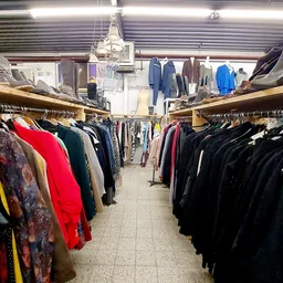 Rekken met tweedehands kleding in verschillende kleuren in een kringloopwinkel