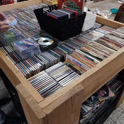 Houten display tafel vol met cd's en dvd's, met een zwarte opbergdoos en losse schijven