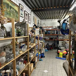 Binnenzicht van kringloopwinkel met houten stellingen vol spullen, bloemen, servies en decoratieartikelen