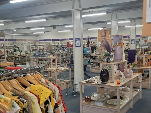 Winkelvloer van kringloopwinkel met kledingrekken, display-tafels met huishoudwaar en decoratie, verlichte plafonds en divers