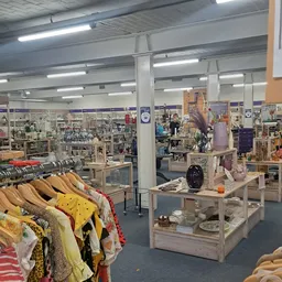 Winkelvloer van kringloopwinkel met kledingrekken, display-tafels met huishoudwaar en decoratie, verlichte plafonds en divers