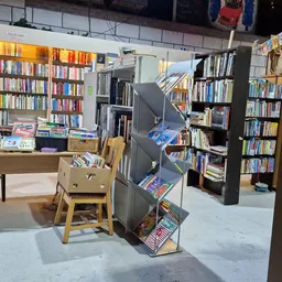 Winkelvloer van kringloopwinkel met boekenrekken, houten meubels en een trap met spullen in het midden