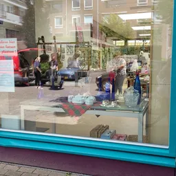Winkelinterieur met glazen displaytafel en uitgestalde spullen, bezoekers zichtbaar buiten
