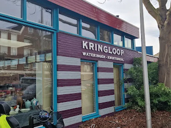 Voorgevel van kringloopwinkel met blauwe kozijnen en paars-witte golfplaten, met winkelnaam KRINGLOOP duidelijk zichtbaar
