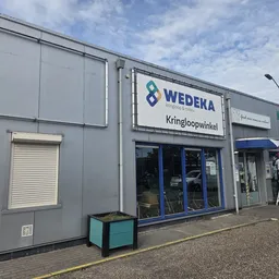 Grijze gevel van Wedeka kringloopwinkel met blauwe entree en winkelnaam zichtbaar