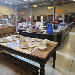 Winkelvloer met eettafel met servies, zitmeubels en huishoudspullen uitgestald