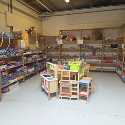 Speelgoedafdeling met houten speelkeuken en dozen speelgoed op houten stellingen langs de wanden