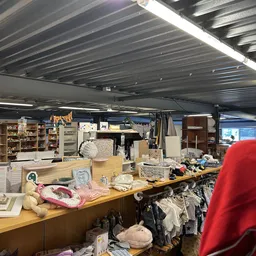 Winkelvloer van kringloopwinkel met tafels vol huishoudartikelen, kleding en diverse spullen