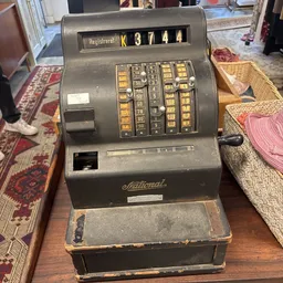 Vintage National kassaregister met gouden toetsen op houten tafel in kringloopwinkel
