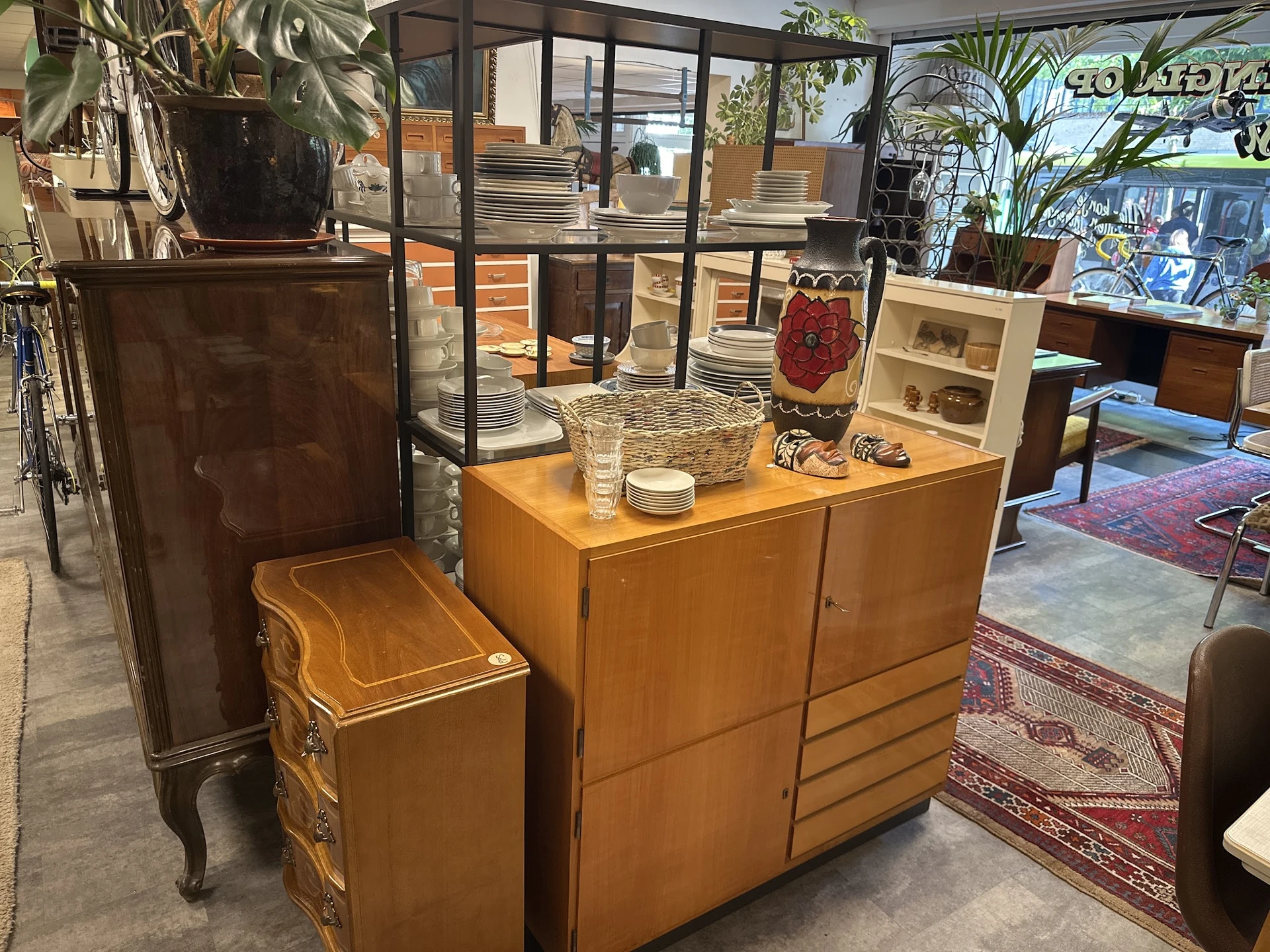 Meubels in de kringloopwinkel: houten kasten, een bijzettafel en een klein stoeltje, met planten en huisraad erop uitgestald
