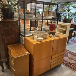 Meubels in de kringloopwinkel: houten kasten, een bijzettafel en een klein stoeltje, met planten en huisraad erop uitgestald
