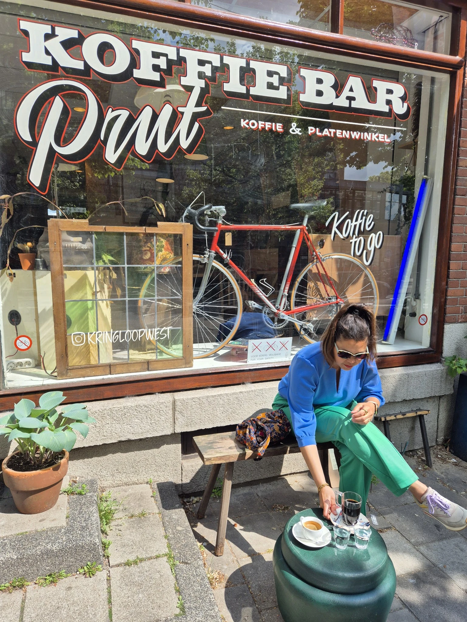 Vrouw zit op terras buiten een winkel met koffie