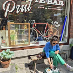 Vrouw zit op terras buiten een winkel met koffie