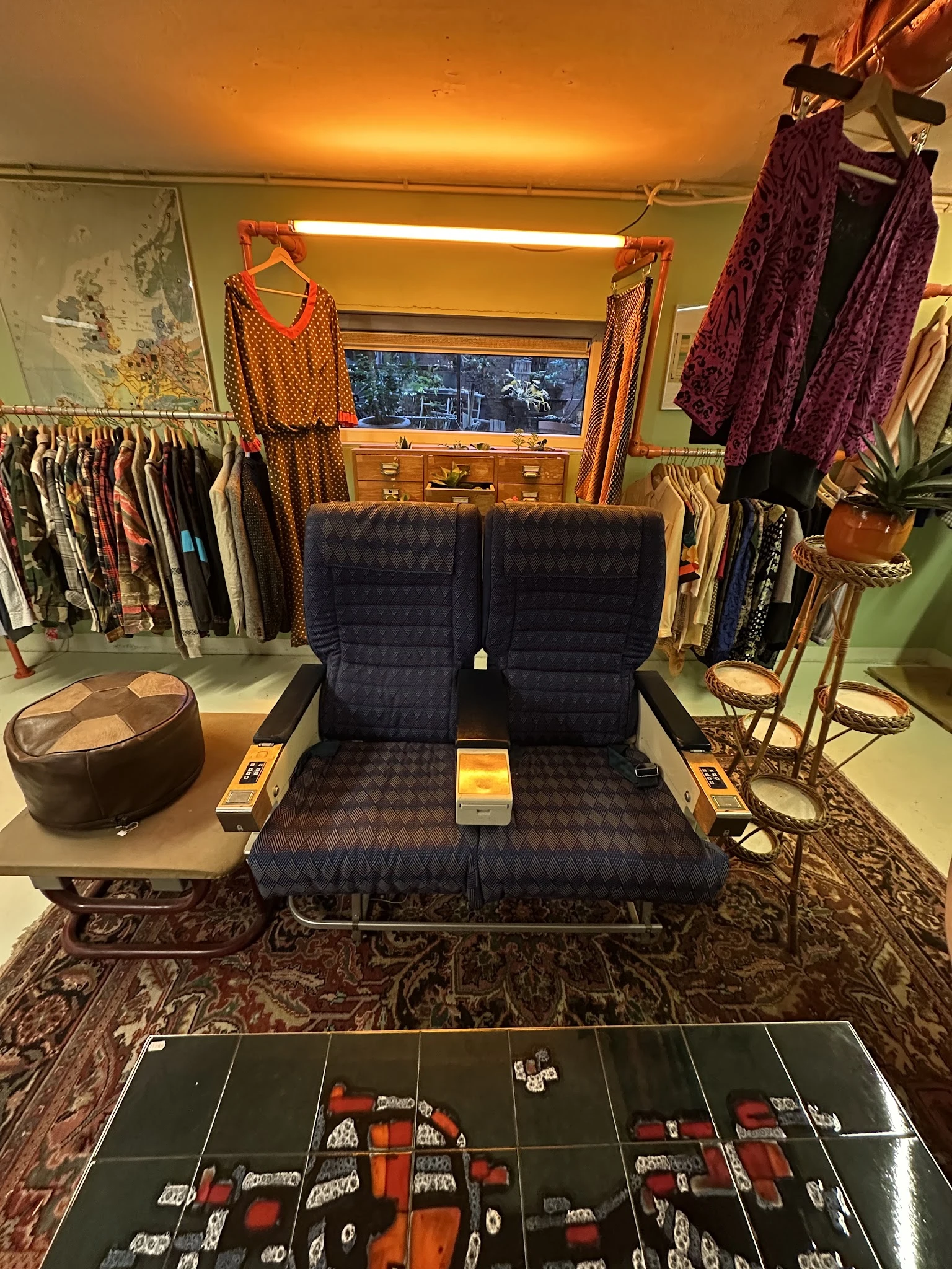 Tweepersoonsbank met donkerblauw patroon in kringloopwinkel, omgeven door kleding en accessoires
