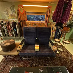Tweepersoonsbank met donkerblauw patroon in kringloopwinkel, omgeven door kleding en accessoires