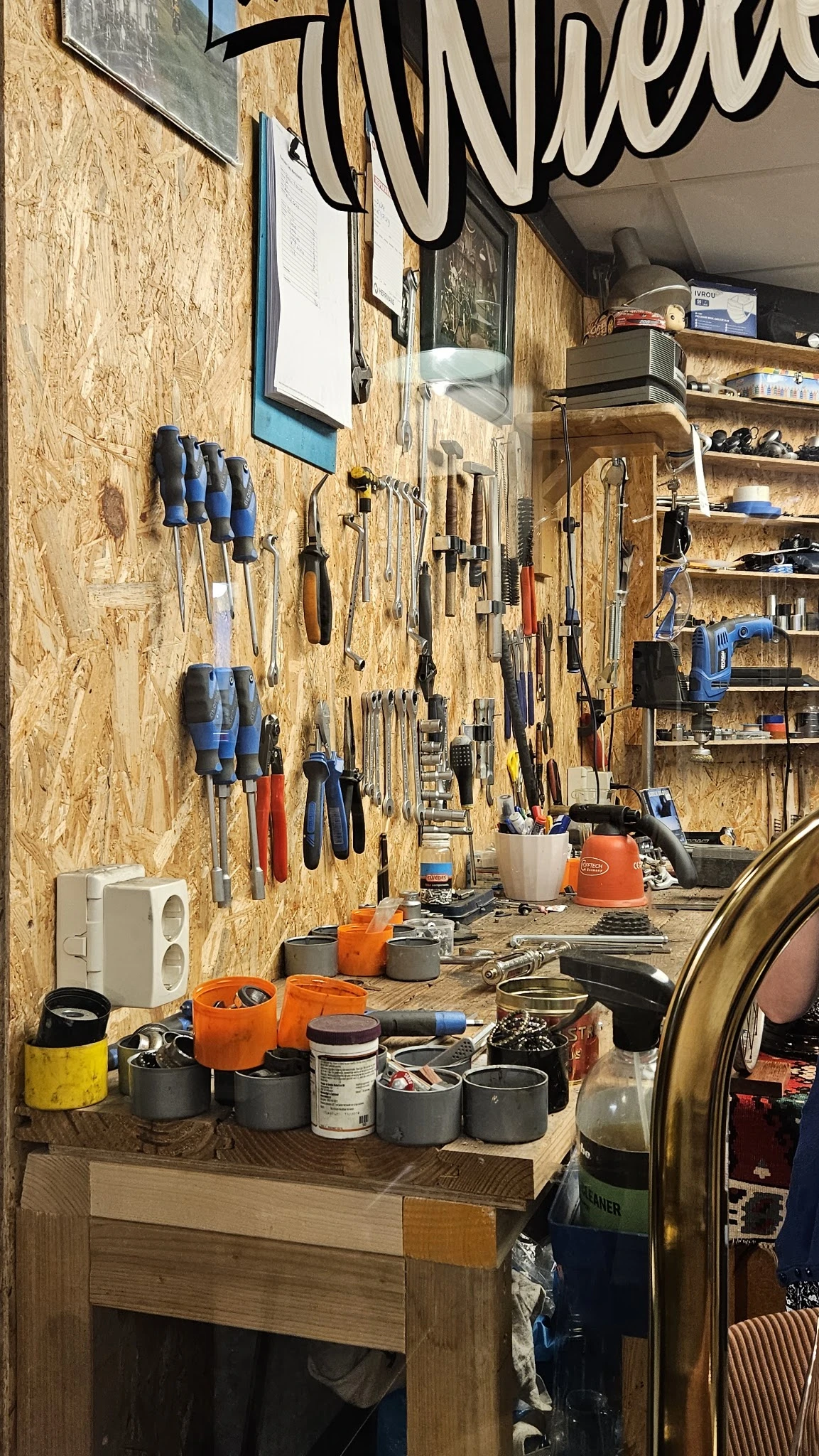 Werkruimte met gereedschapswand vol hangers, schroevendraaiers en ander gereedschap, workbench met oranje gereedschapskist