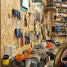 Werkruimte met gereedschapswand vol hangers, schroevendraaiers en ander gereedschap, workbench met oranje gereedschapskist