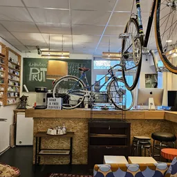 Winkelbinnenruimte met houten toonbank, fietsen aan het plafond, boekenrekken, groene schoolbord en zithoek met oranje access
