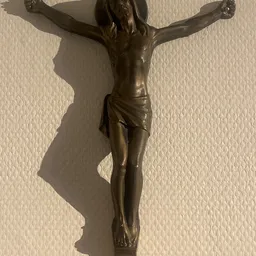 Bronzen crucifix tegen beige muur, met duidelijke schaduwwerking