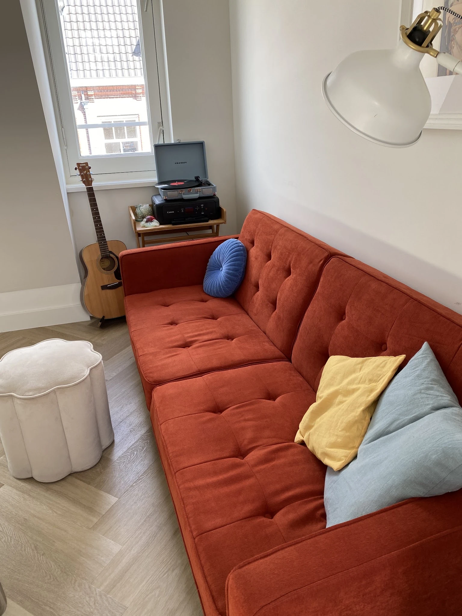 Oranje getufted zitbank met blauwe en gele kussens, gitaar en platenspeler op achtergrond