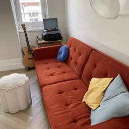 Oranje getufted zitbank met blauwe en gele kussens, gitaar en platenspeler op achtergrond