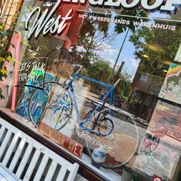 Blauwe fiets tegen raam van winkel met graffiti en reclames