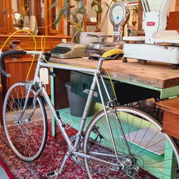 Werkplek met twee fietsen, houten tafel, computer en apparatuur in een kringloopwinkel